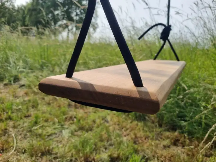 Schaukelbrett aus Eiche an schwarzen Kletterseilen über einer Wiese mit hohem Gras