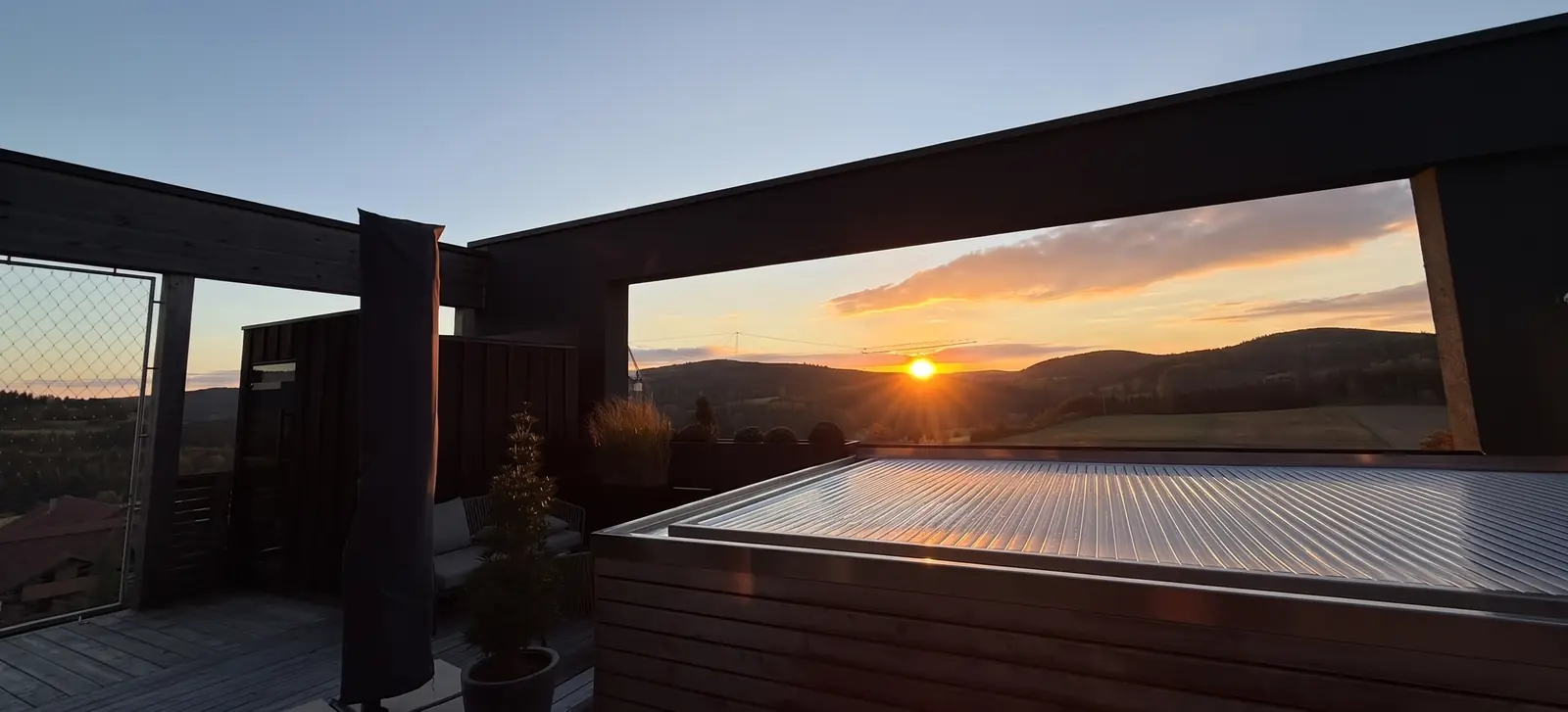 Dachterrasse der Pool Suite 501 im Ulrichshof bei Sonnenuntergang: vorn der abgedeckte Pool, durch einen dunklen Rahmen der Blick über die Hügel des Bayerischen Waldes, am Horizont ein Baukran